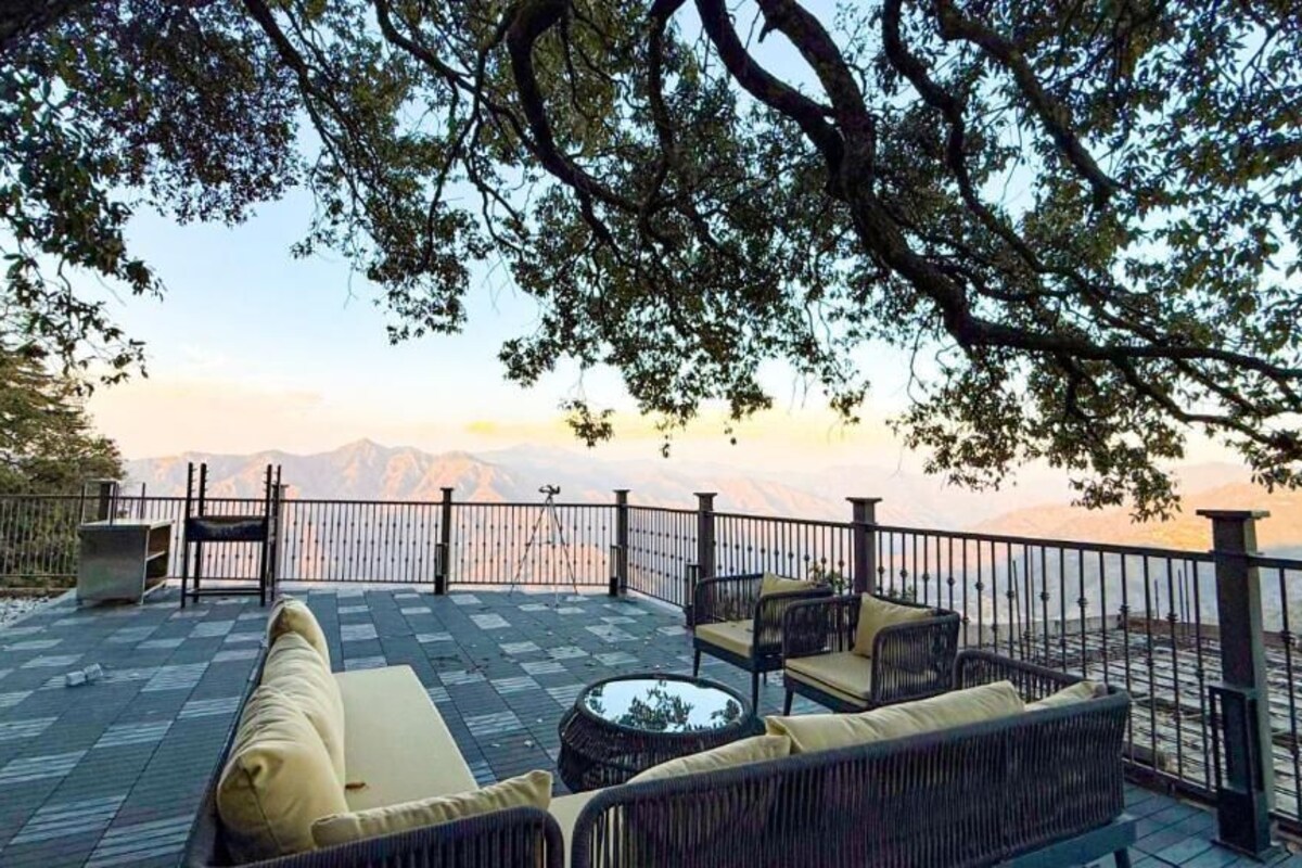 An outdoor seating area with a view of mountains, furnished with sofas and chairs, and a railing around the perimeter.