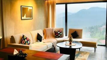 Habitación de hotel moderna con un conjunto de sofás, una mesa de comedor y vistas a montañas a través de ventanas amplias.