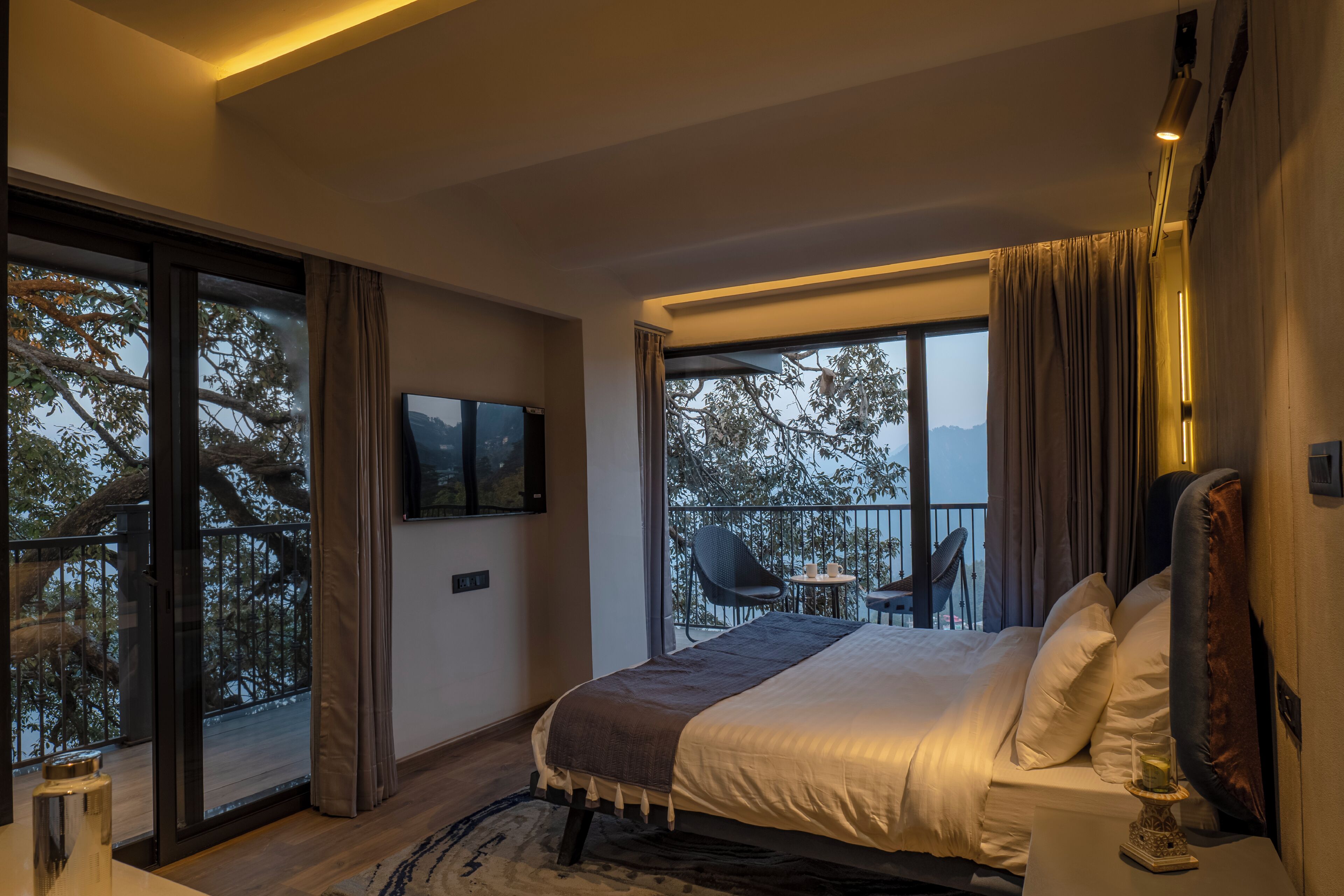 Un dormitorio moderno con una cama grande, televisor y balcón con mesa y sillas.
