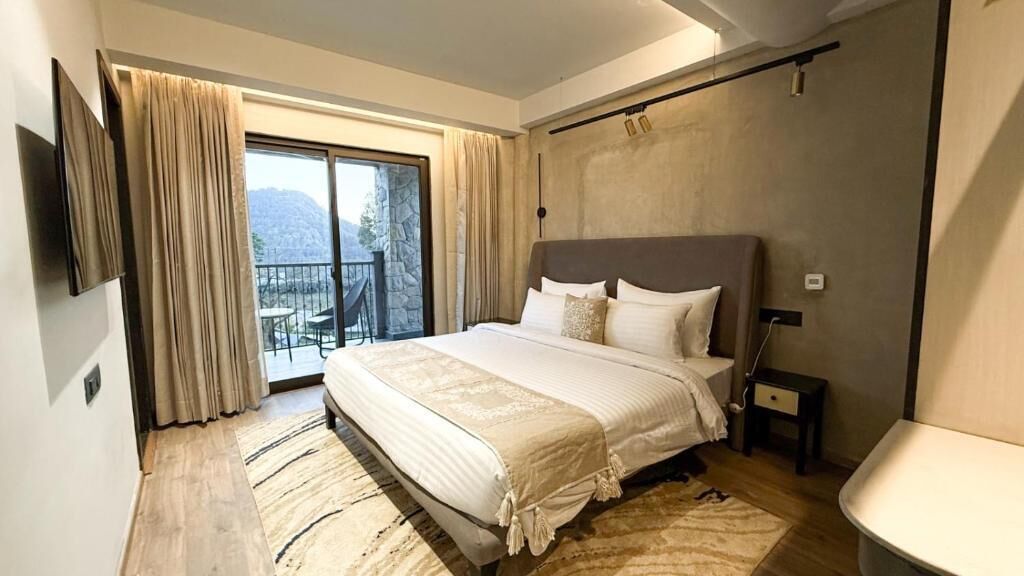A bedroom with a large bed, a TV mounted on the wall, and a balcony with curtains.