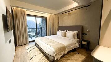 A bedroom with a large bed, a TV mounted on the wall, and a balcony with curtains.
