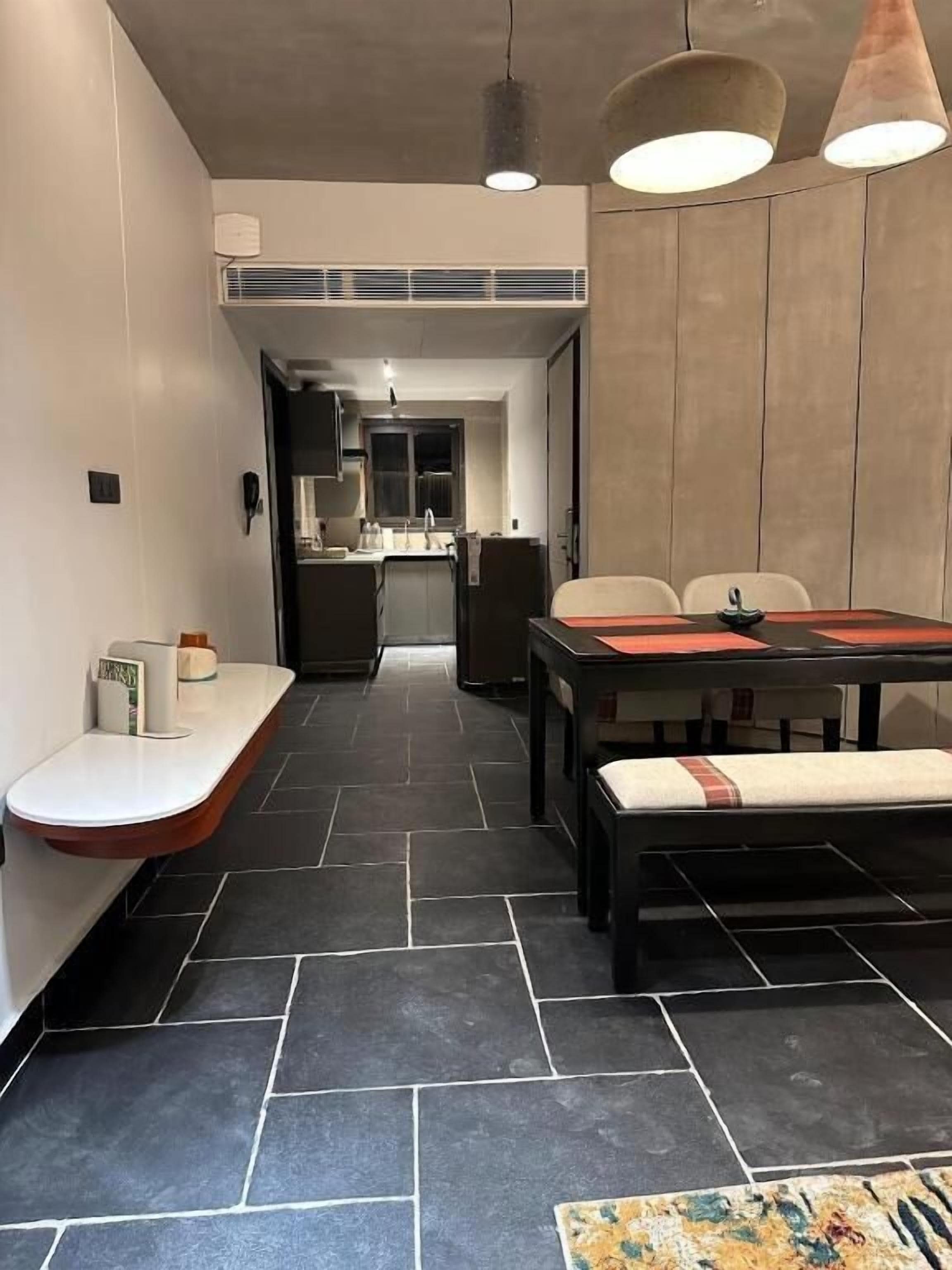 Un comedor moderno con una mesa larga, sillas y un banco. Se ve una cocina al fondo.