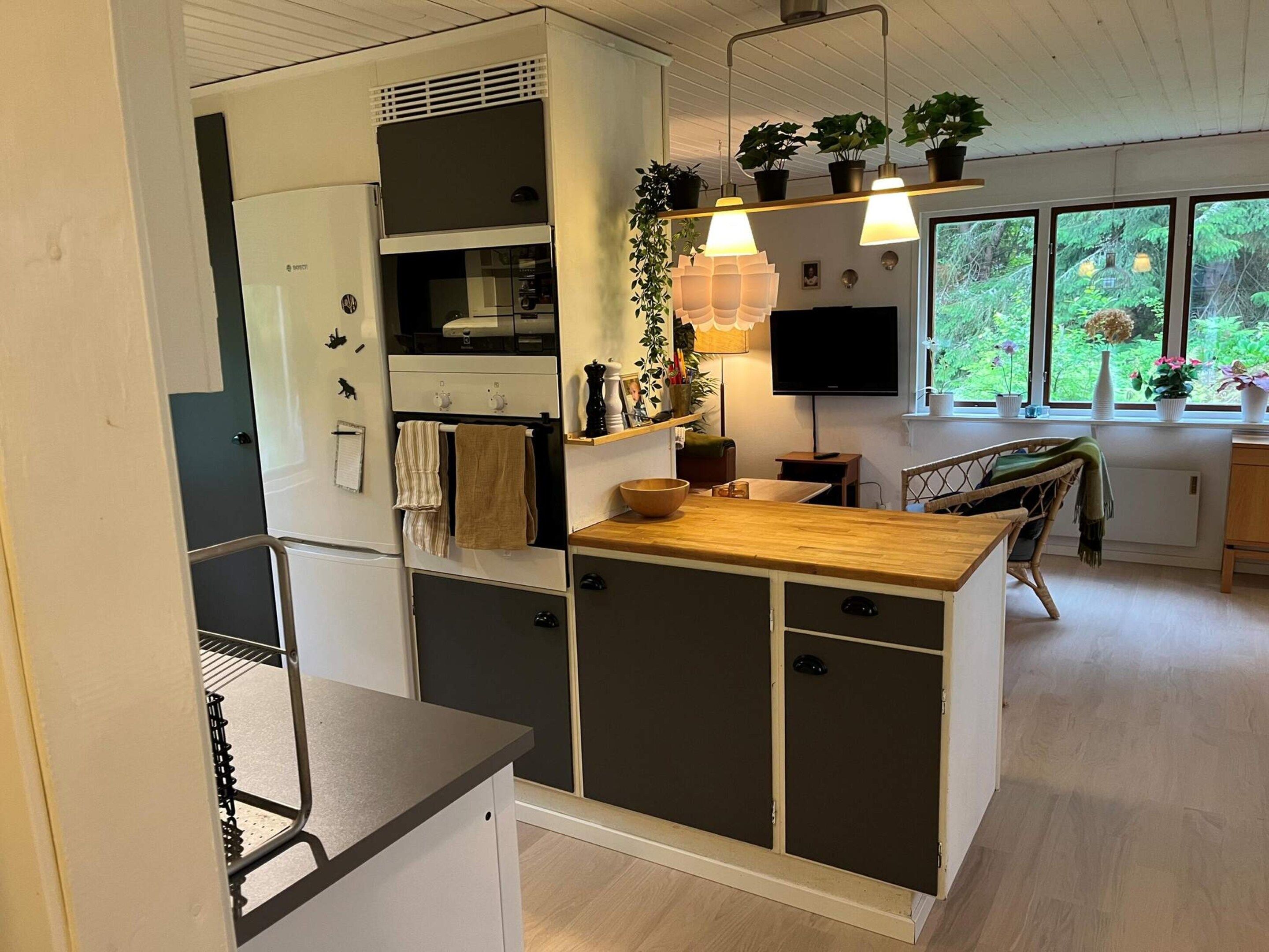 Een compacte keuken met een ingebouwde oven, een houten aanrechtblad en een eethoek met een stoel.