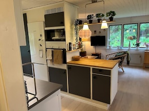 Cozinha compacta com forno embutido, bancada de madeira e espaço de jantar com uma cadeira.