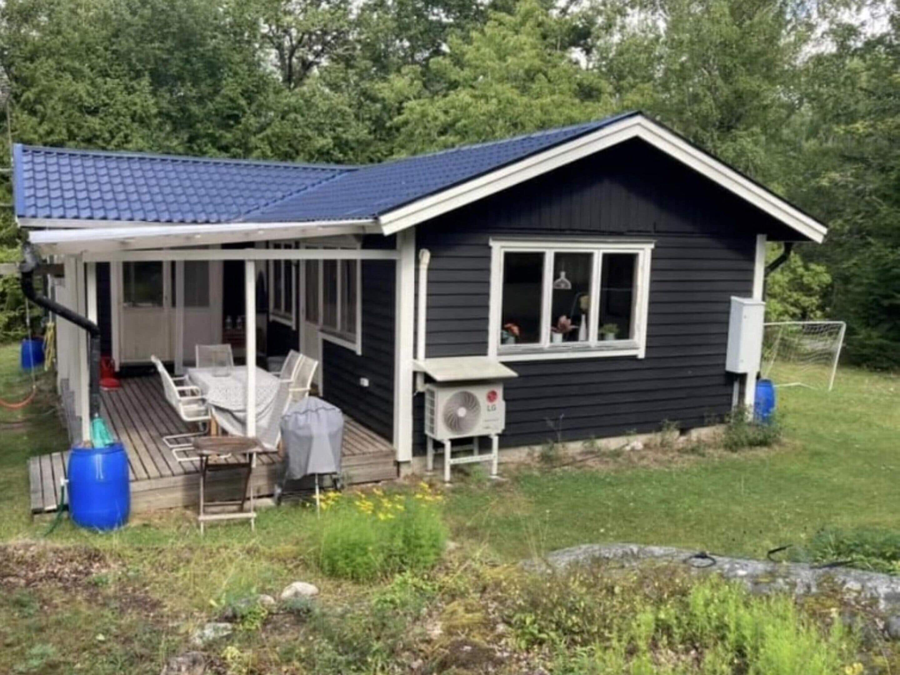 A small house with a covered porch, a table and chairs, and an air conditioning unit.