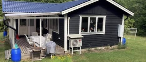 A small house with a covered porch, a table and chairs, and an air conditioning unit.