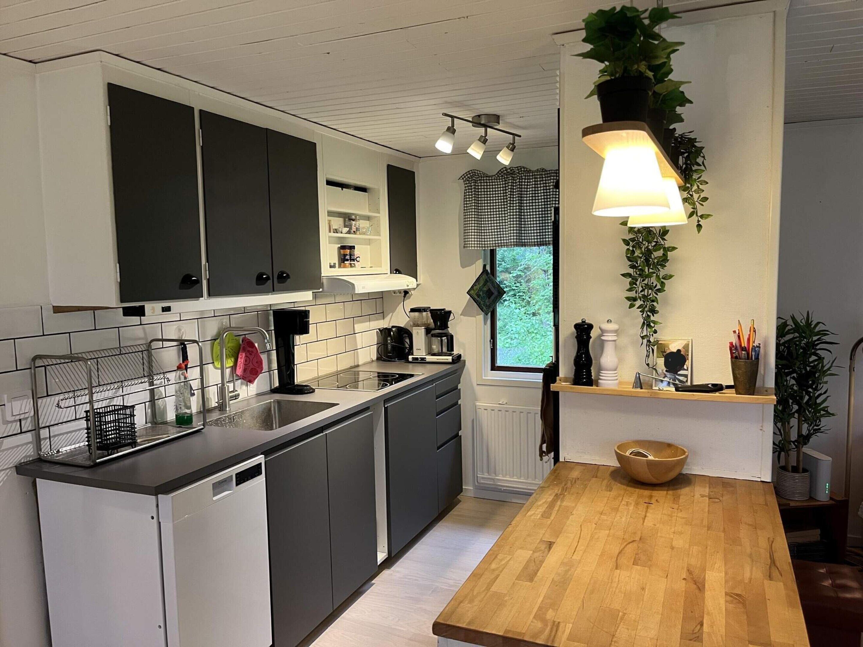 A modern kitchen with a wooden countertop, black cabinets, and a window with a view.