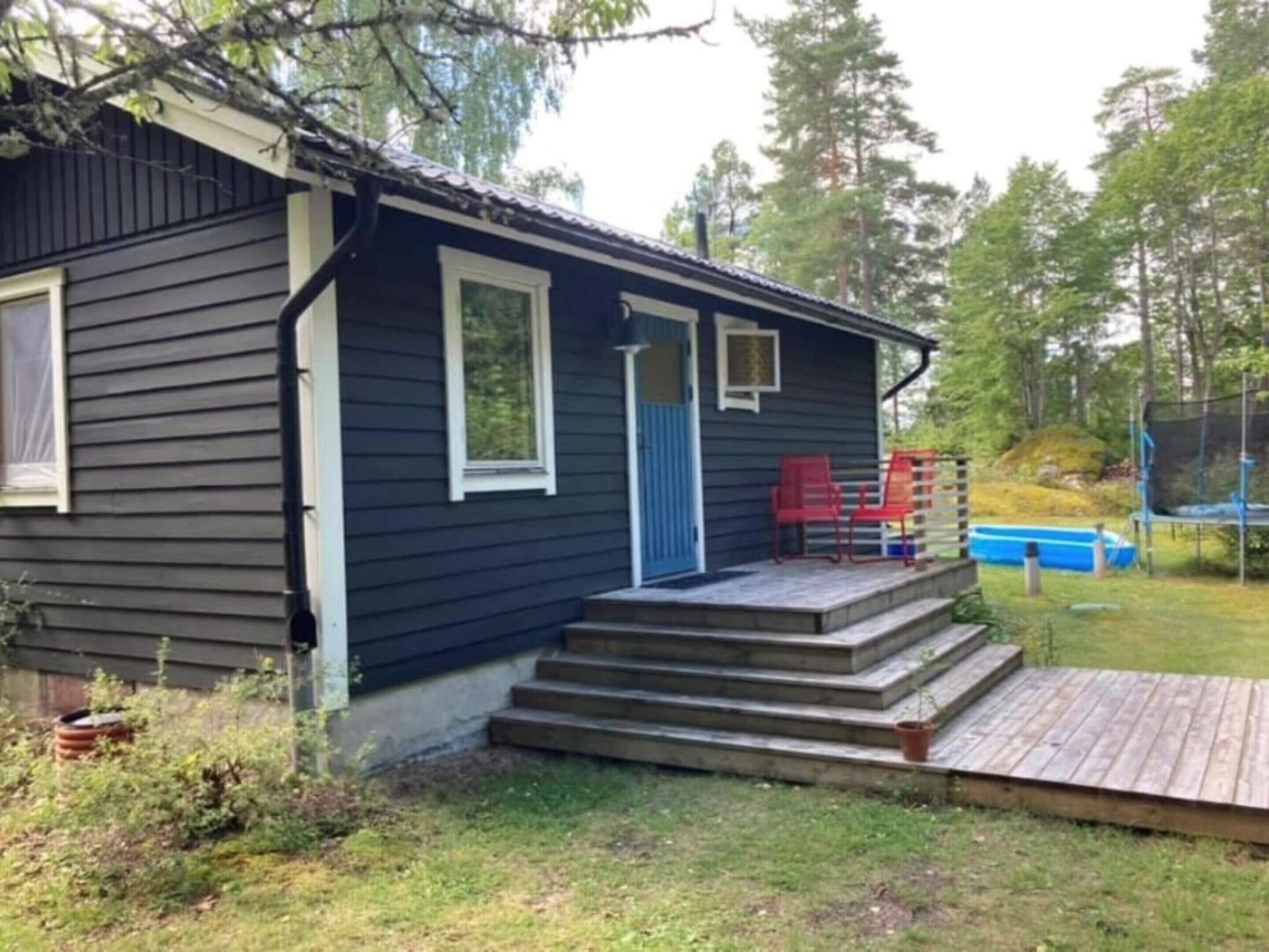 A small cabin with a wooden deck, a blue door, and a small porch with red chairs.