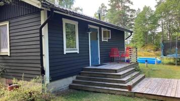 A small cabin with a wooden deck, a blue door, and a small porch with red chairs.