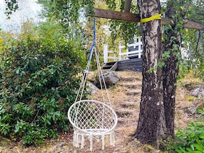 A white swing chair suspended from a tree, surrounded by greenery and a wooden fence. - 4 Star Holiday Home in Malmkoping (Malmkoping)