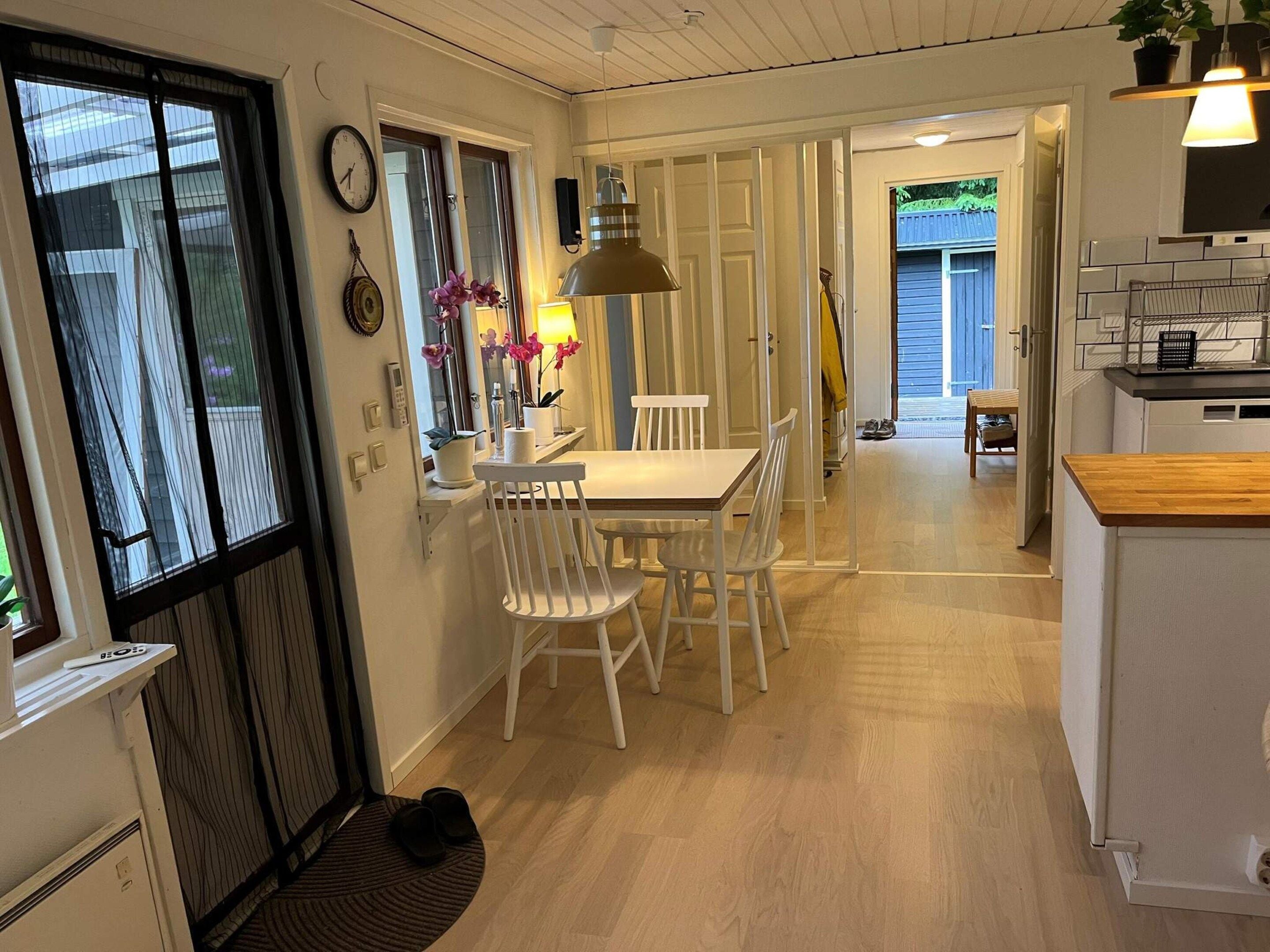 A dining area with a table and chairs, a clock on the wall, and a window with curtains.