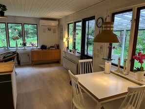 Cozinha moderna com armários de madeira, uma mesa de jantar e cadeiras. Janelas oferecem vista para o verde lá fora.
