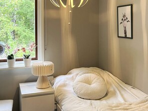 A bedroom with a bed, a bedside table, a lamp, a window with plants, and a framed picture on the wall. - 4 Star Holiday Home in Malmkoping (Malmkoping)