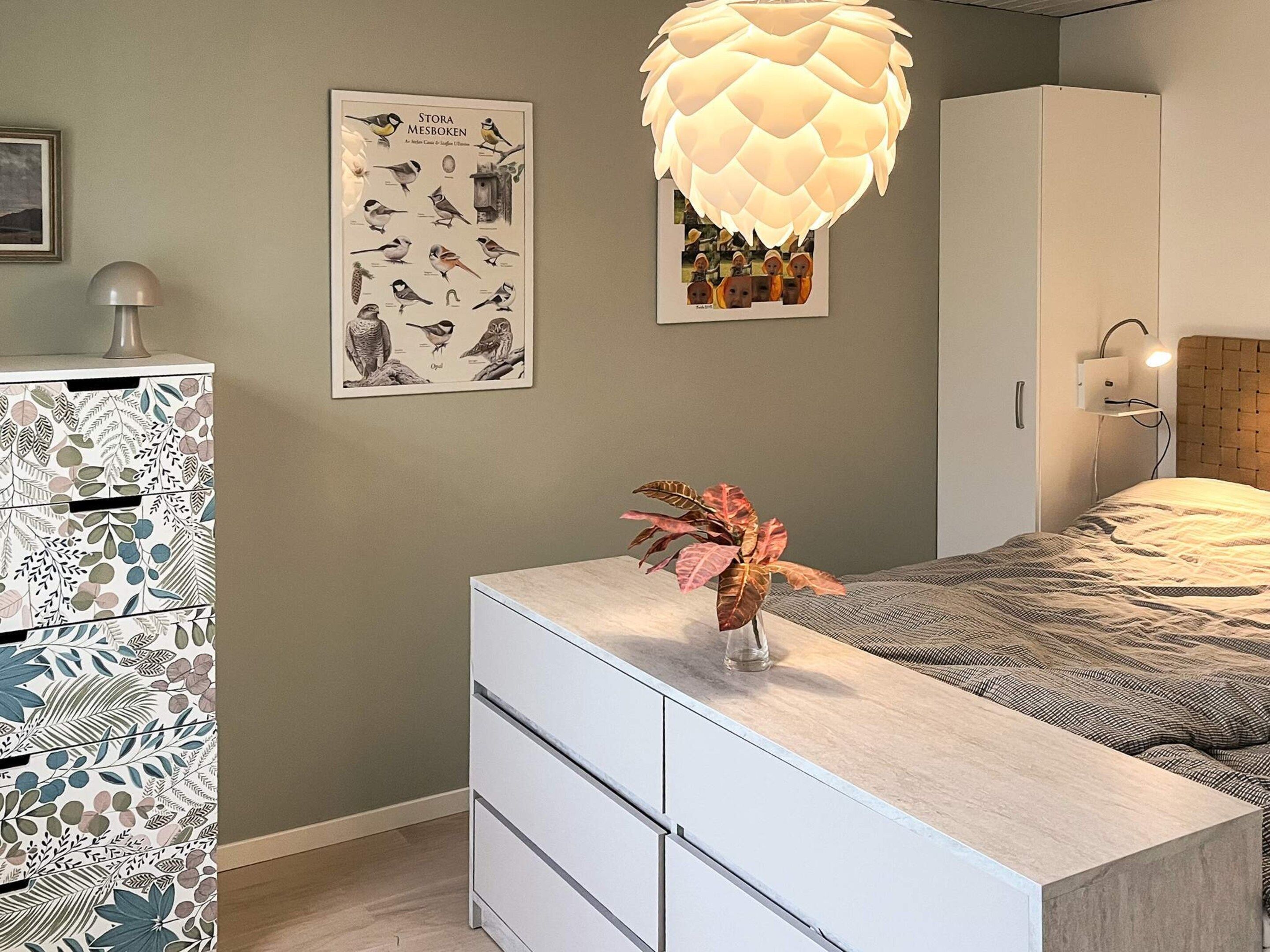 A bedroom with a bed, a dresser, a wall-mounted lamp, and a poster of birds.