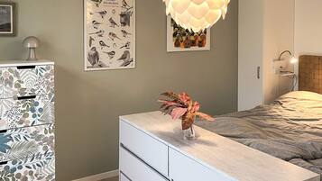A bedroom with a bed, a dresser, a wall-mounted lamp, and a poster of birds.