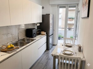 A modern kitchen with white cabinets, a marble backsplash, and a dining area with a table set for two. - Domus Acquedotti (Roma)