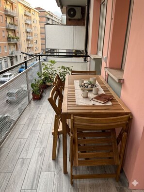Ein Holztisch mit Stühlen auf einem Balkon mit Blick auf eine Stadtansicht.
