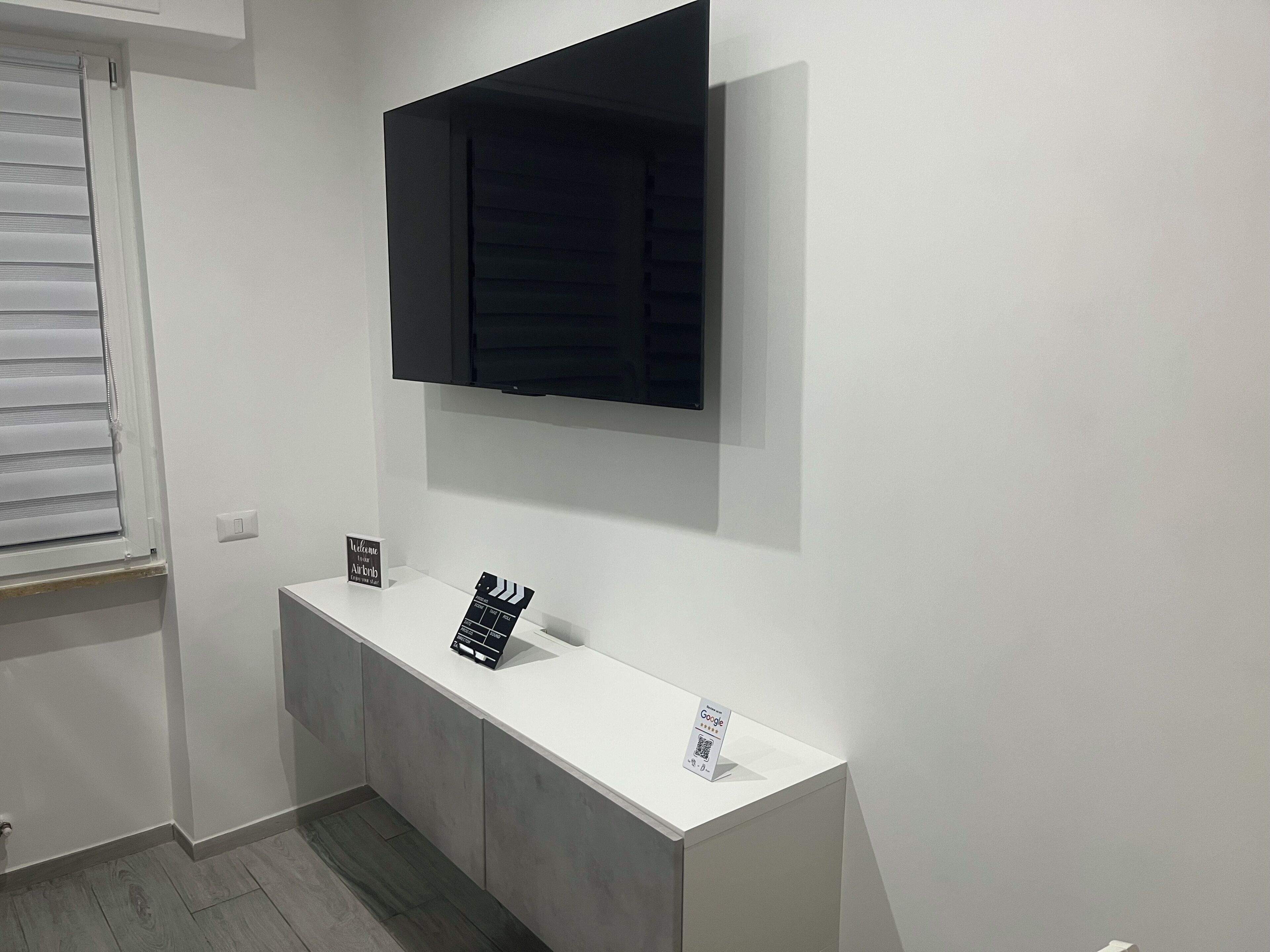 A room with a white console table, a flat-screen TV mounted above it, and a window with blinds.