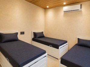 A bedroom with three single beds, a wooden ceiling, and an air conditioning unit. - ZEST STAYS GOREGAON WEST (Mumbai)