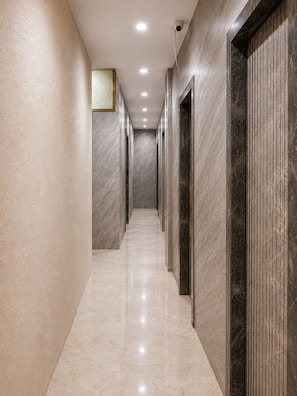 A corridor with marble walls and floors, leading to doors with a dark, textured finish.