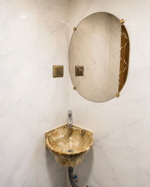 A bathroom with a marble sink, a round mirror with a geometric pattern, and two wall-mounted light switches.