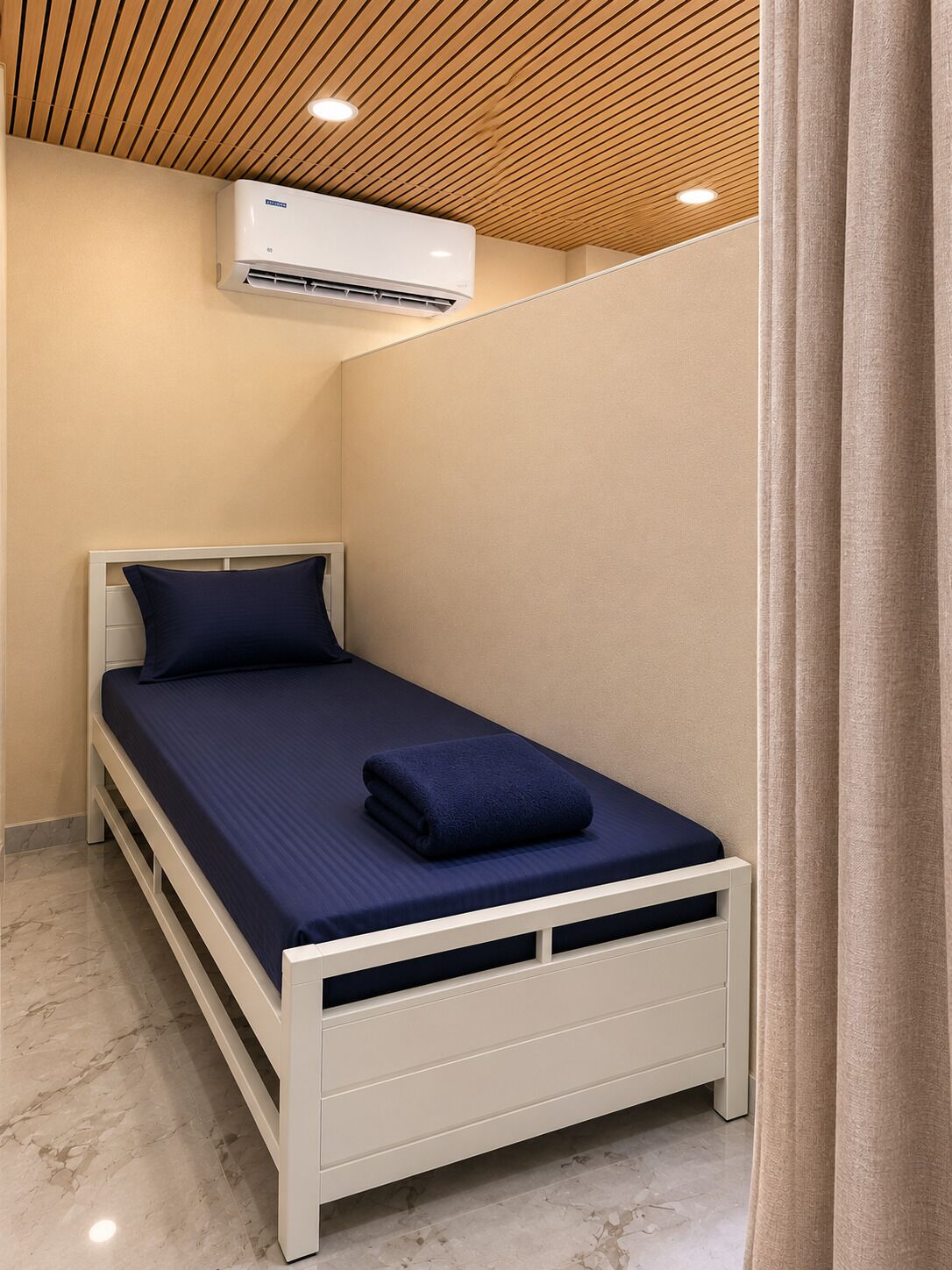 Un letto singolo con struttura bianca e biancheria da letto blu scuro, una parete bianca, un soffitto in legno e un condizionatore d'aria a soffitto.