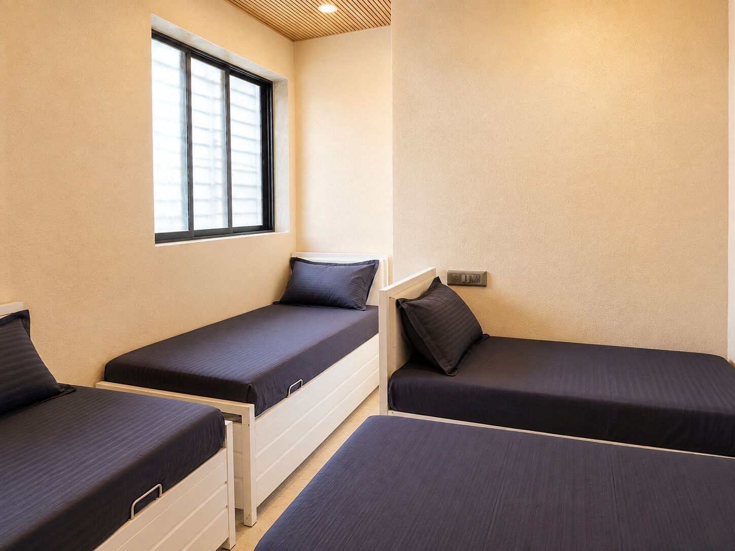 Una habitación con tres camas individuales, una ventana y un enchufe.