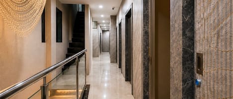 A modern hotel corridor with a glass railing, marble flooring, and a decorative light fixture.