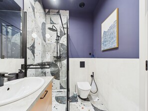 Un baño moderno con cabina de ducha de vidrio, un lavabo blanco y un inodoro.
