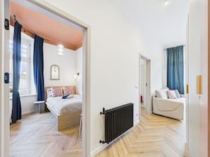 Un dormitorio con cama, radiador, ventana con cortinas y sofá.