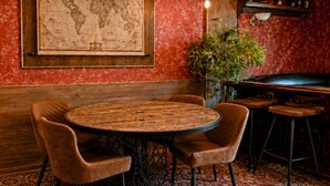 Una mesa redonda de madera con cuatro sillas acolchadas, un mapa mundial en la pared, una lámpara colgante y una zona de bar con taburetes.