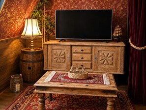 Een kamer met een televisie op een houten kast, een lamp, een klein scheepsmodel en een gevlochten mand op een tafel.