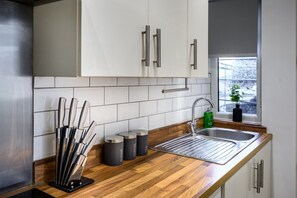Uma cozinha moderna com armários brancos, uma pia de aço inoxidável e bancada de madeira.
