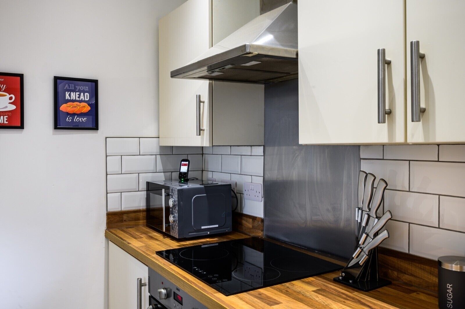 A modern kitchen with white cabinets, a stainless steel range hood, a built-in oven, and a coffee machine.