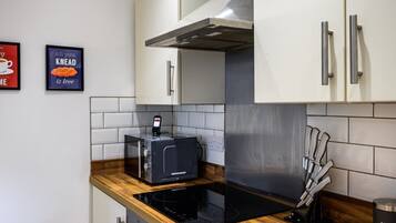 A modern kitchen with white cabinets, a stainless steel range hood, a built-in oven, and a coffee machine.