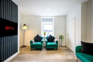 Een moderne woonkamer met twee groene fauteuils, een vloerlamp en een groot raam.