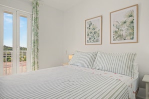 A bedroom with a bed, two framed botanical prints on the wall, a window with a view, and a curtain. - El Rincón de la Mancebía Apartment (Alcalá de los Gazules)