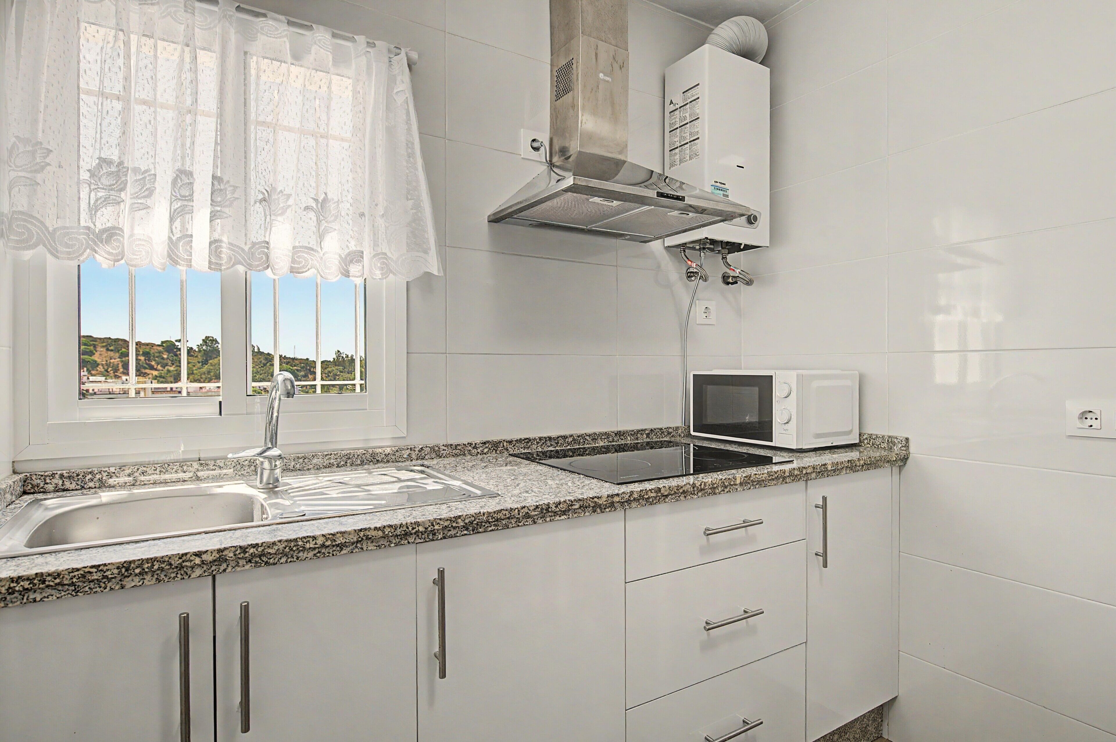 Una cocina con ventana, pileta, microondas y estufa.