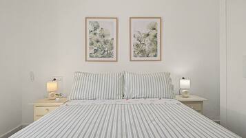 A hotel room with a bed, two nightstands, a lamp, a power outlet, and two framed botanical prints on the wall.