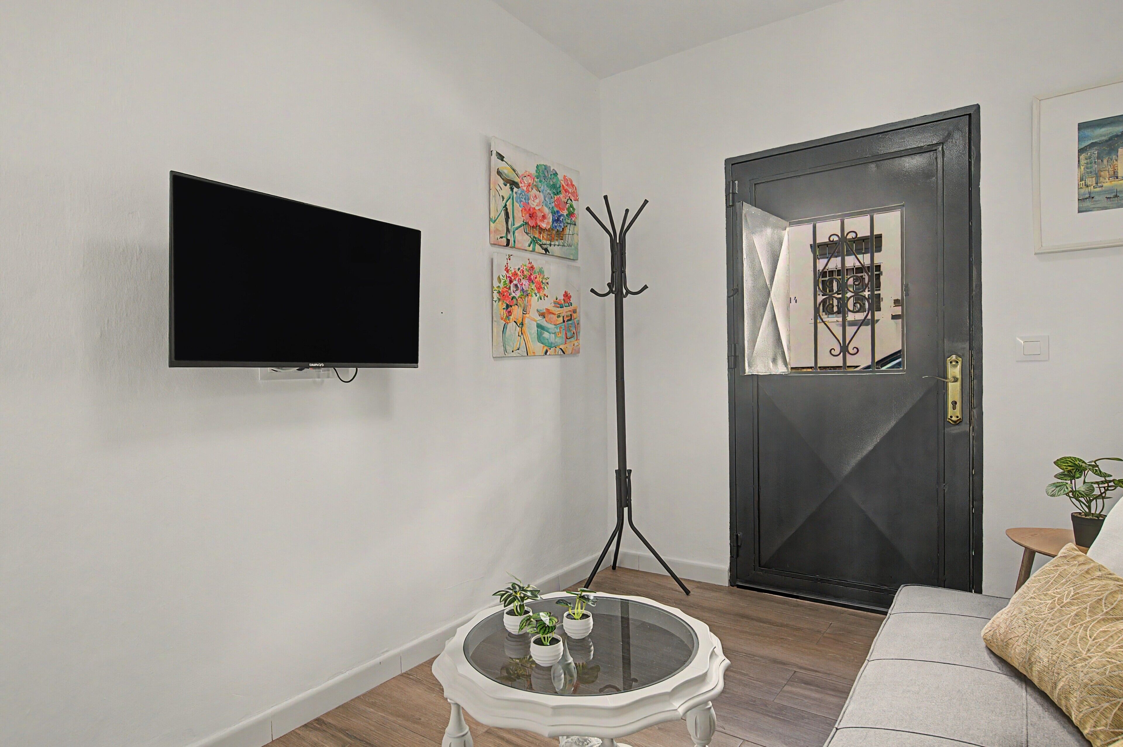 A living room with a flat-screen TV mounted on the wall, a coat stand, and a door with a decorative metal gate.