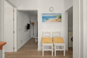 Un corridoio con un quadro raffigurante una spiaggia, un orologio a parete e una lavatrice sullo sfondo.