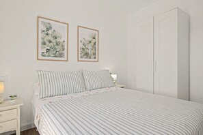 Una camera da letto con un letto, due stampe incorniciate con motivi botanici, un comodino con una lampada e un armadio.
