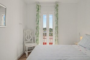 Una camera da letto con un letto, una sedia, una finestra con tende e vista sull'esterno.