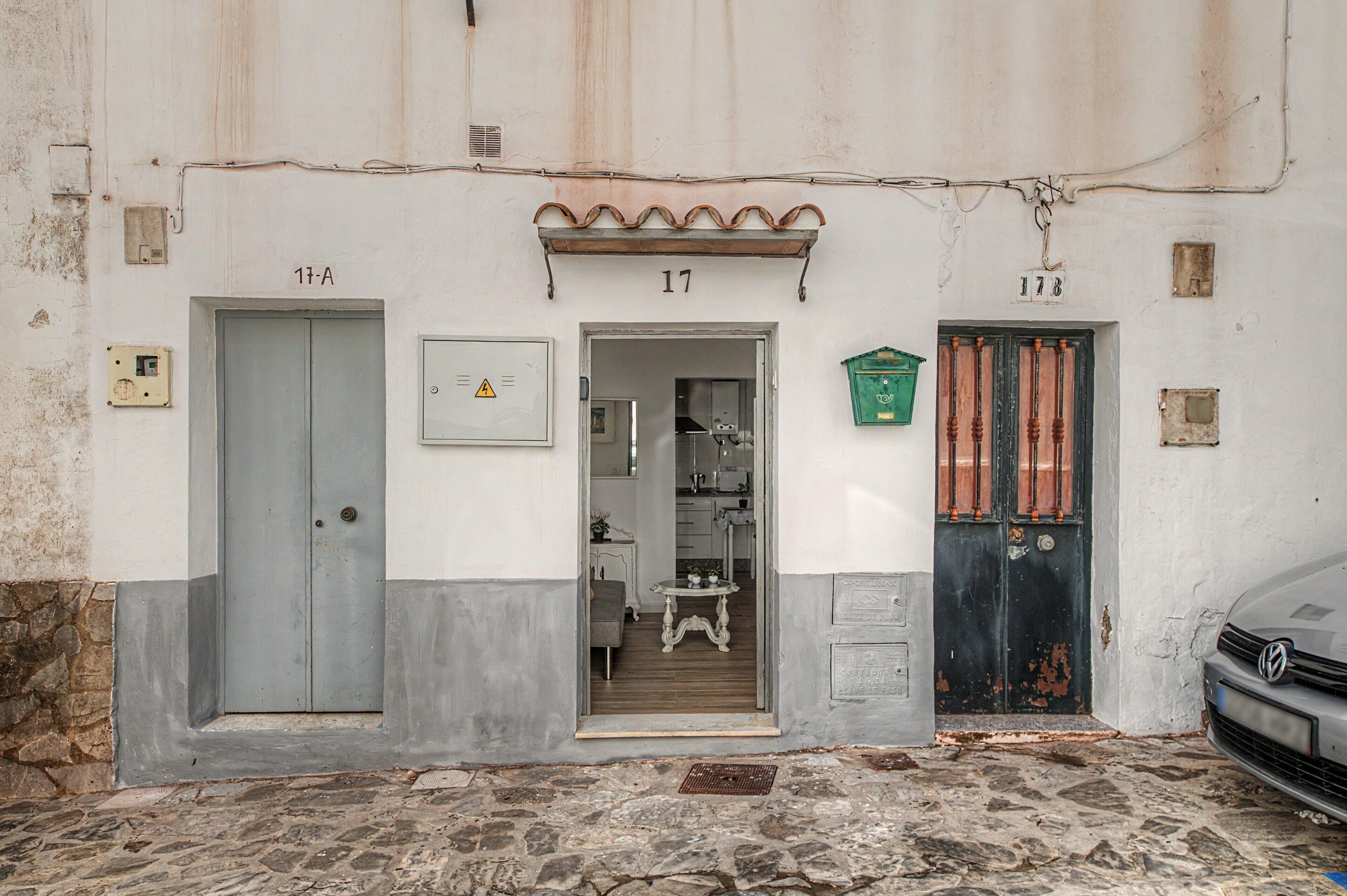 A building with three numbered doors, a visible entrance, and a car parked in front.
