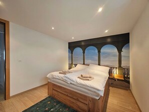 Un dormitorio con cama, piso de madera, mesita de noche y un mural en la pared con arcos.