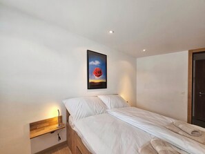A bedroom with a bed, a bedside table, a wall-mounted painting, and a door. - Aramis EG Appartement/Fewo Appartement/Fewo by Interhome (Saas-Fee)
