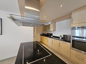 Una cocina moderna con extractor de vidrio, electrodomésticos de acero inoxidable y armarios de madera clara.