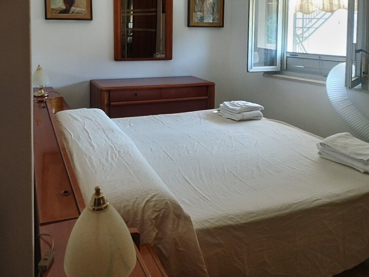 Een hotelkamer met een bed, nachtkastje, lamp, raam met uitzicht en een deur.