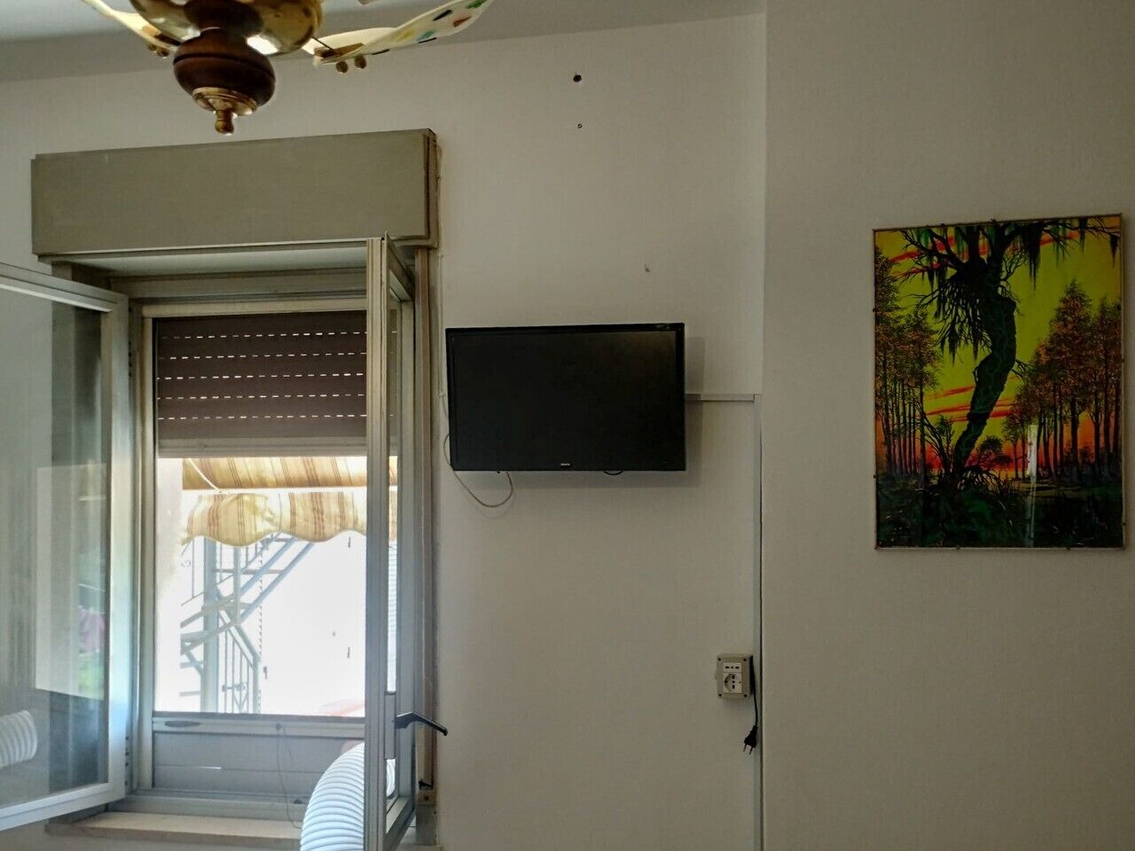 Une pièce avec un téléviseur fixé au mur, une fenêtre avec des stores et une porte donnant sur l’extérieur.