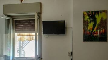 Une pièce avec un téléviseur fixé au mur, une fenêtre avec des stores et une porte donnant sur l’extérieur.